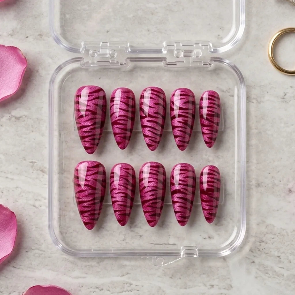Ten pink coffin-shaped press-on nails with a dark magenta zebra stripe pattern, displayed in a clear plastic case on a light marble surface with pink petals.