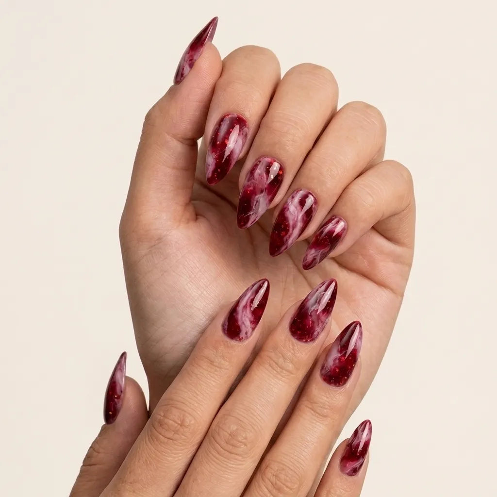 A close-up of a hand with long, almond-shaped nails painted in a glossy deep burgundy red and white marble pattern, set against a solid light beige background.
