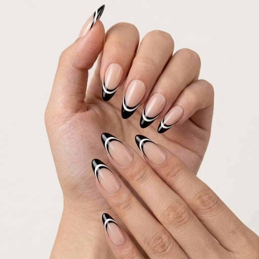 A set of 10 false press-on nails in a clear plastic case, featuring a nude pink base with a black and white French tip design. The case is styled on a beige surface with small decorative props including white flowers, pearls, and a gold ring.