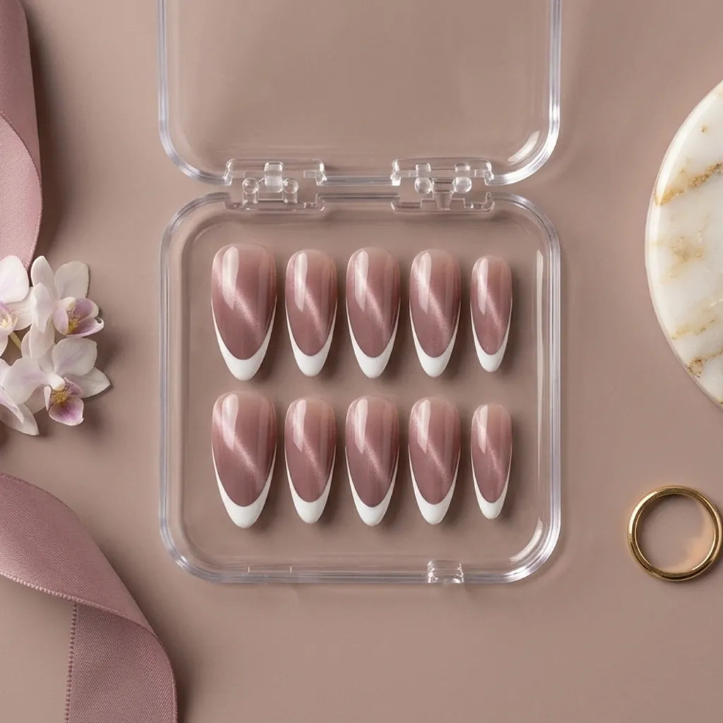 A set of ten false press-on nails in a clear plastic case, arranged on a dusty pink background with decorative flowers, a ribbon, and a ring.