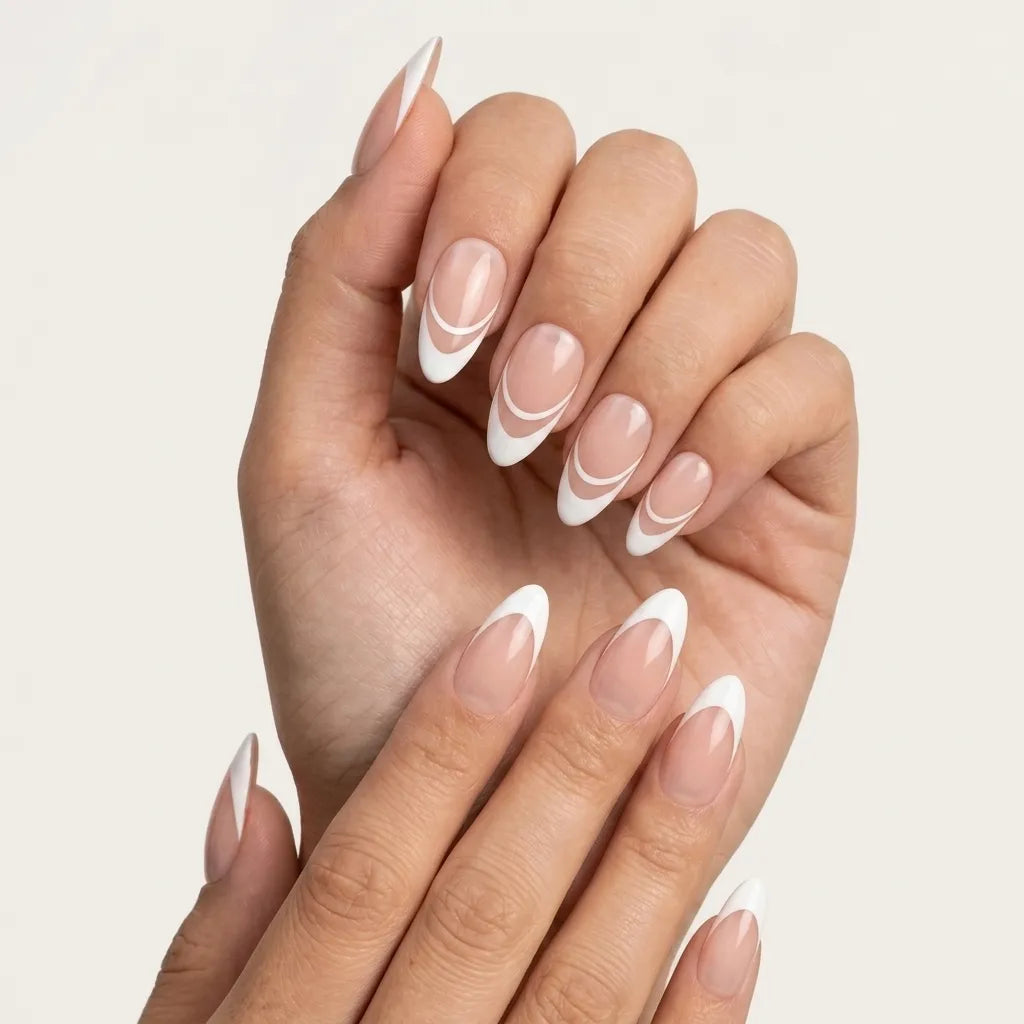 A close-up of a hand with long almond-shaped nails styled in a classic French manicure with a white curved stripe detail on a nude pink base, set against a clean off-white background.