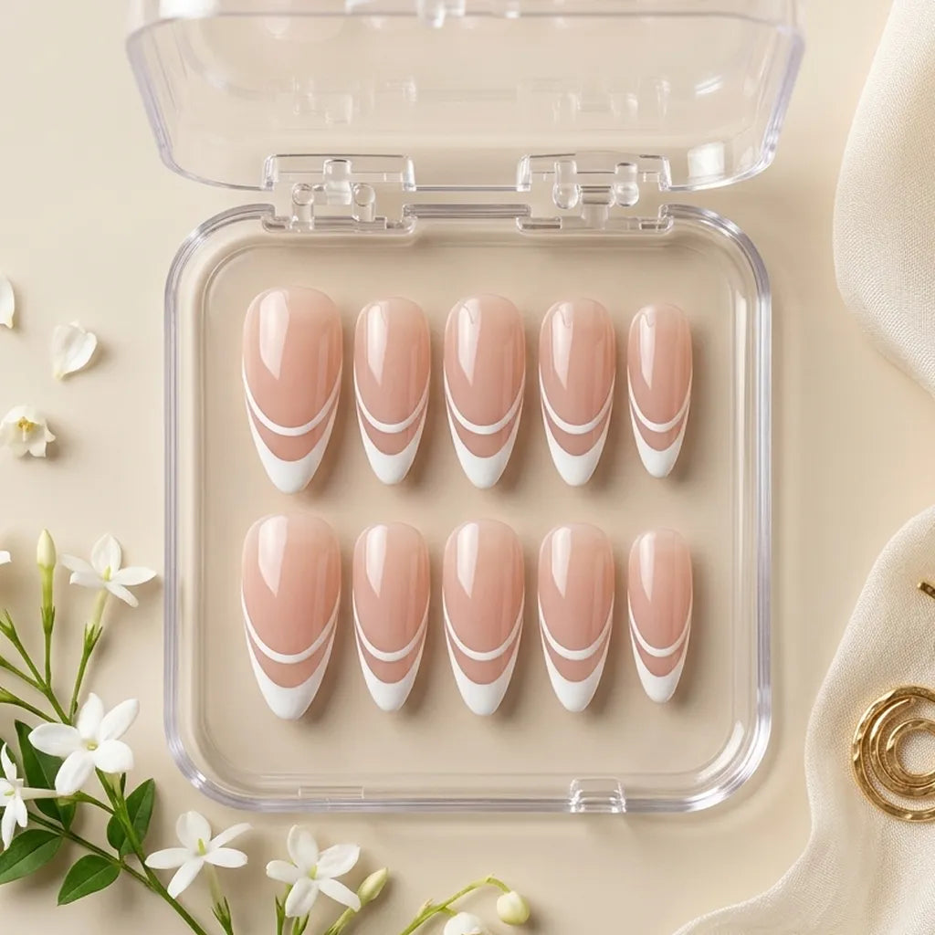 A set of ten false press-on nails in a clear plastic case, featuring a nude pink base with a white French tip and curved white stripe design, styled on a beige surface with small white flowers.