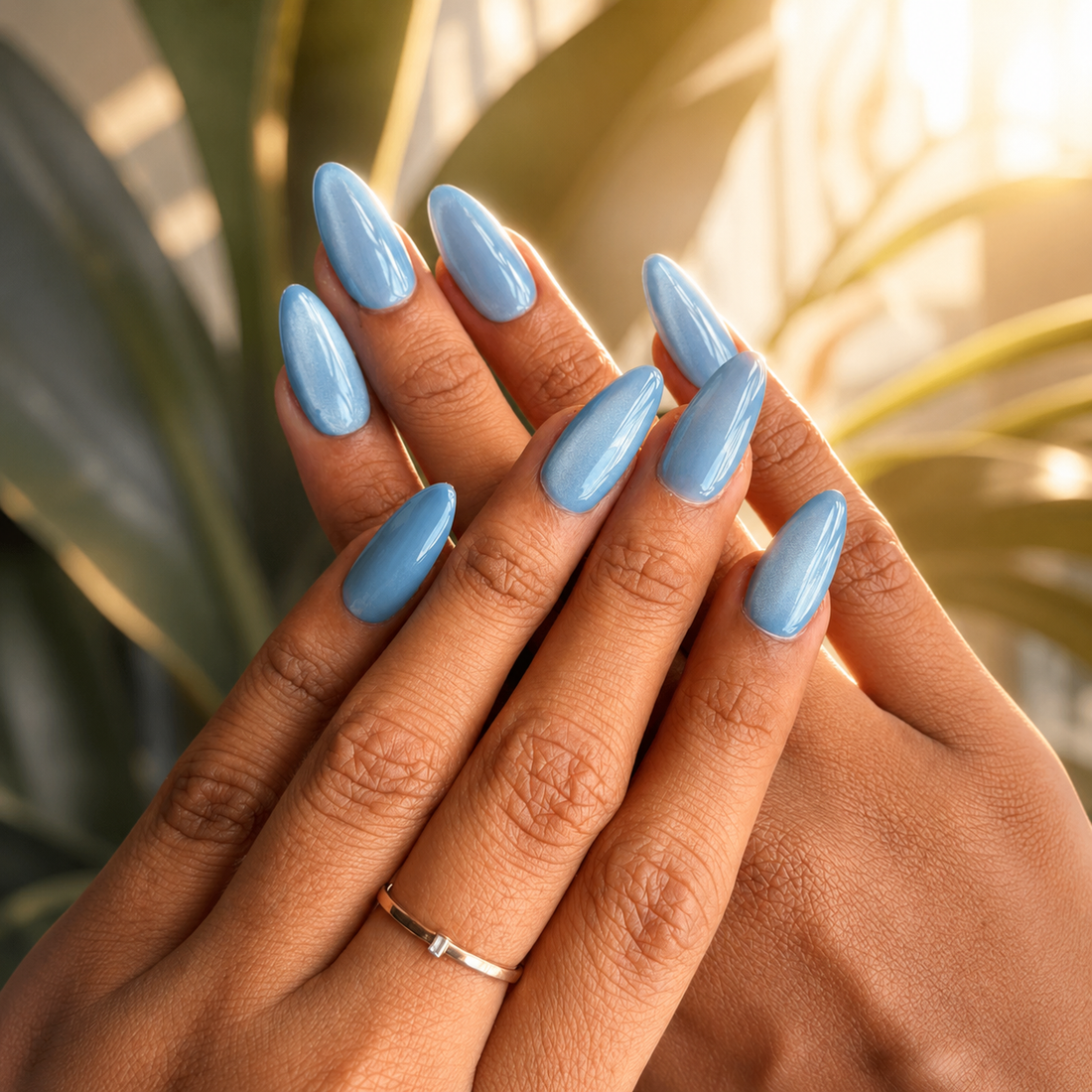 A set of ten false press-on nails in a metallic slate blue color, displayed inside an open clear plastic case on a marble surface with a blue fabric and silver ribbon prop.