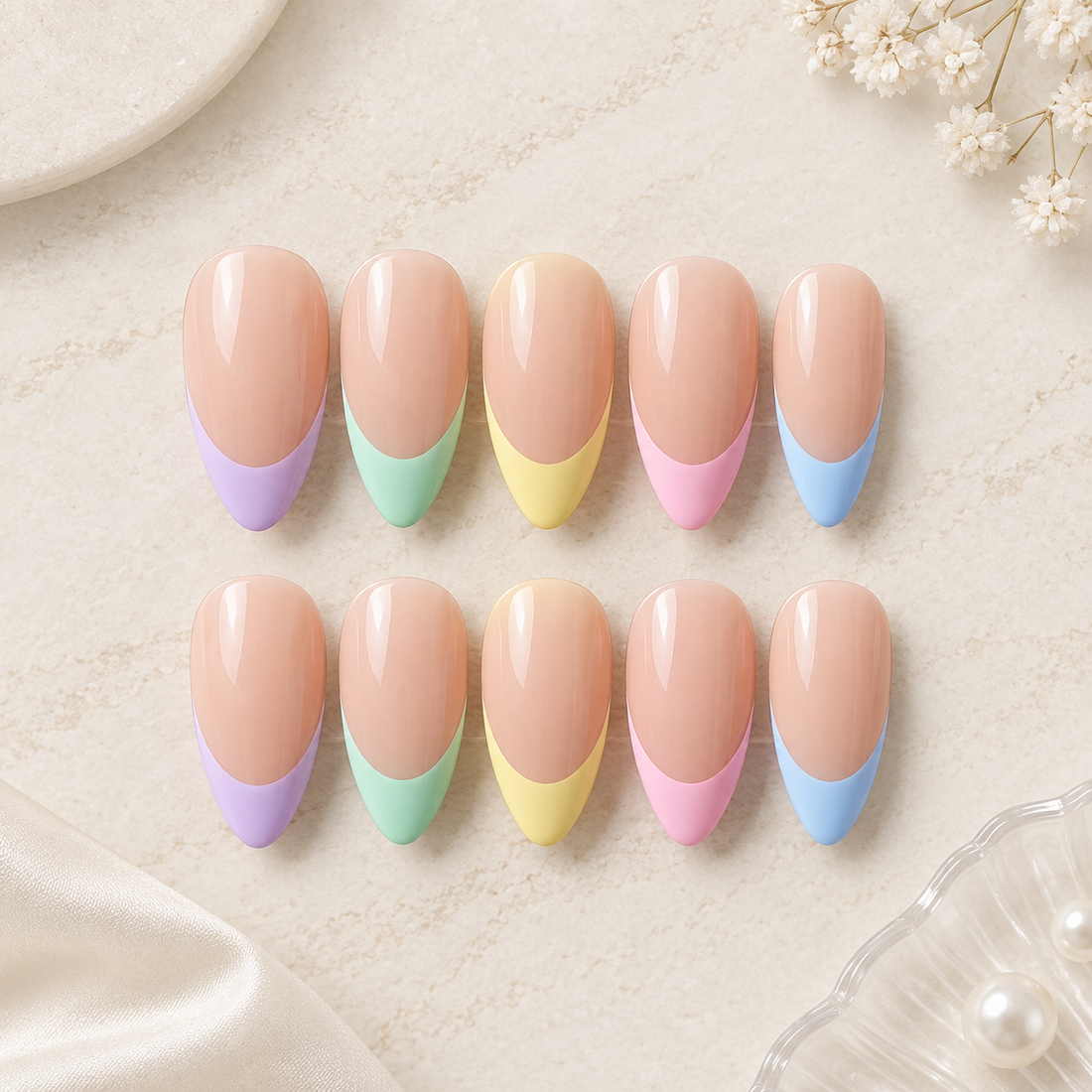 Ten false press-on nails arranged in two rows on a light beige textured surface. Each nail has a nude peach top half and a pastel French tip half: purple, mint green, pale yellow, pink, and light blue.